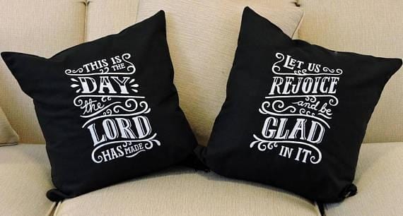 A picture of both pillows with the phrase "This Is The Day The Lord Has Made" on one and "Let Us Rejoice And Be Glad In It" on the other. Both pillows are black with white writing.